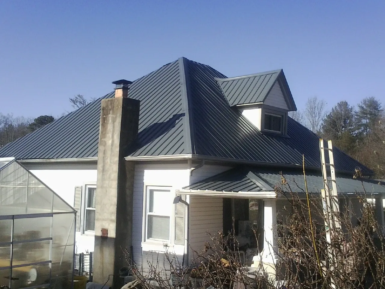 Dark blue standing seam metal roof on a white farmhouse with dormer in Jerseyville