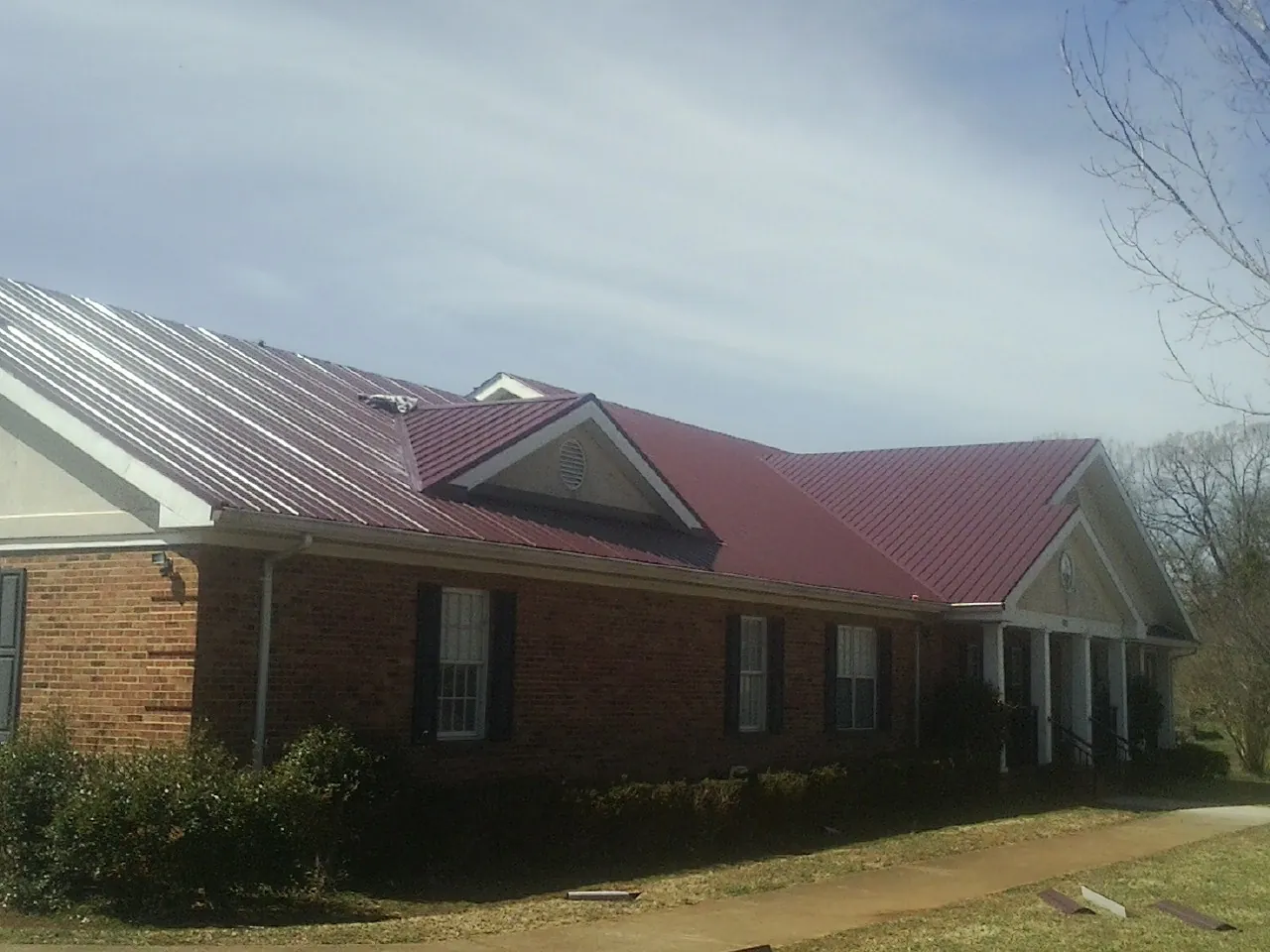 Red metal roof with gabled entries on a long brick building, from a Hail Damage Roof Repair job in Jerseyville