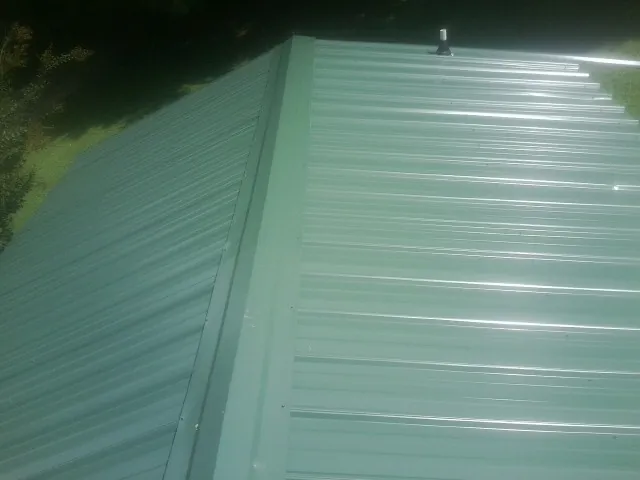 New green metal panels meeting at the ridge of a roof — Flat Roof Repair work by our crew in Jerseyville