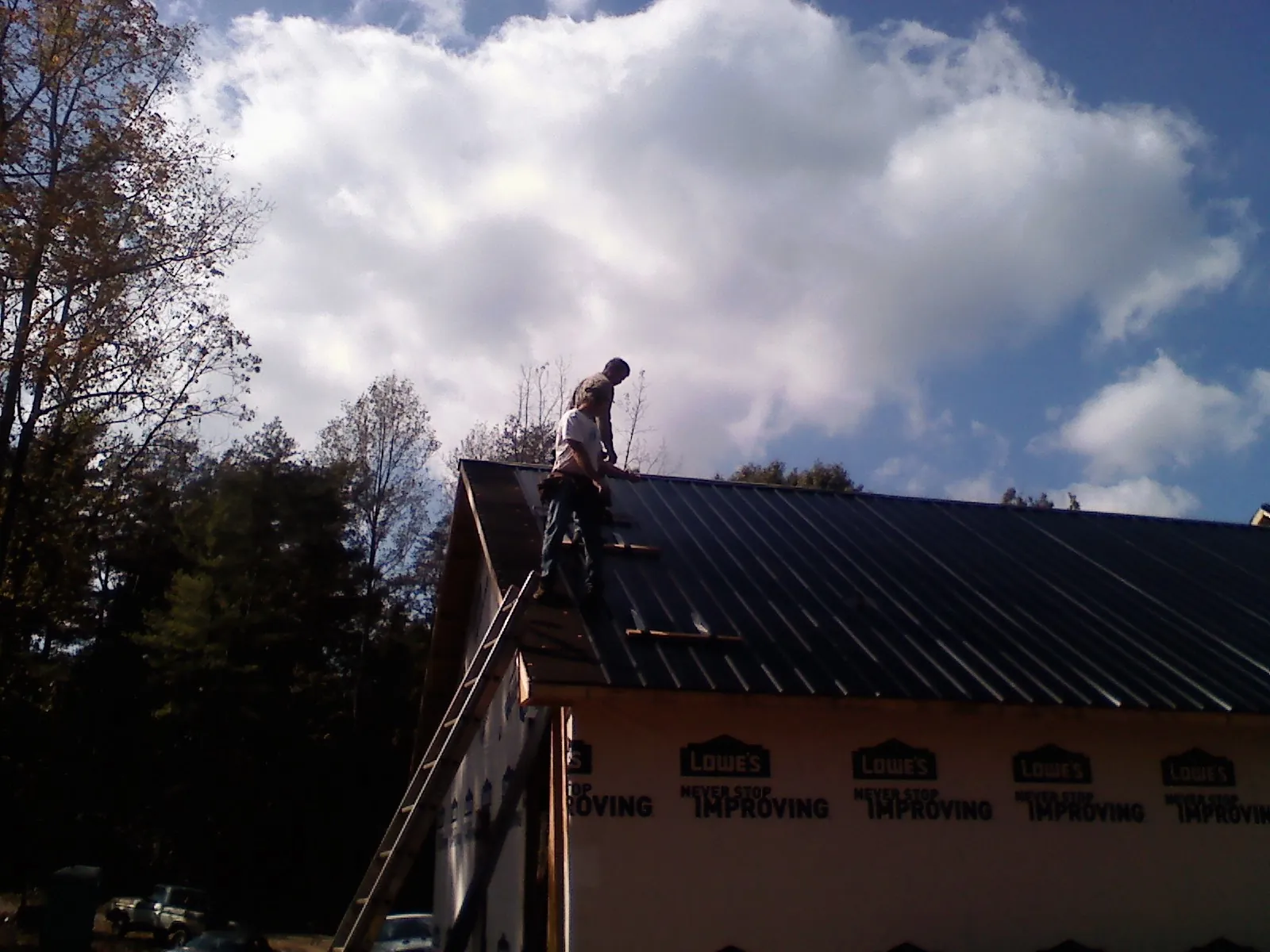Roofer fastening dark metal panels high against a cloudy sky, from a Roof Inspection job in Jerseyville