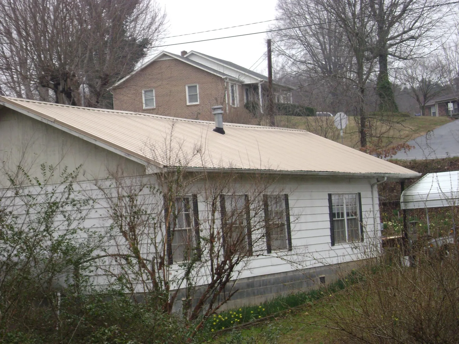 Tan metal roof on a white sided house set into a hillside — Commercial Roofing by Roofing Brothers in Jerseyville