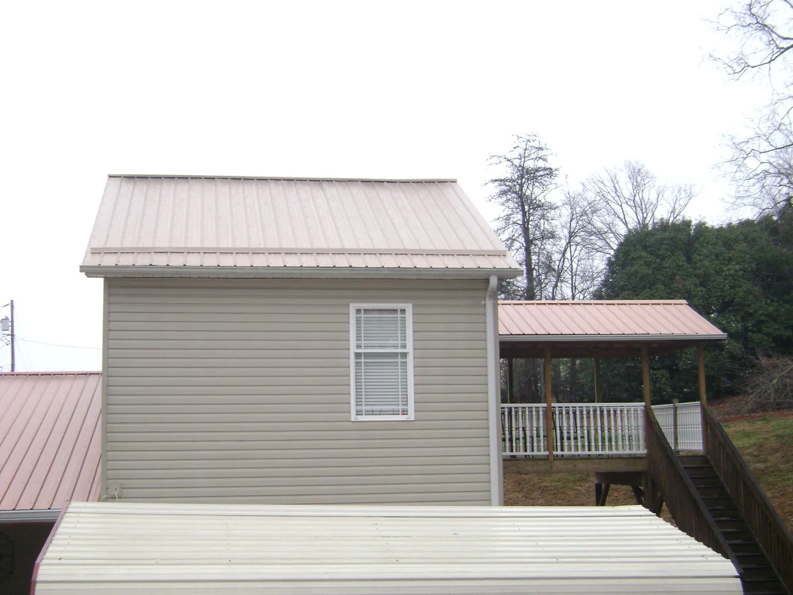 Tan metal roofs on a two story addition and attached porch, from a Roof Replacement job in Jerseyville